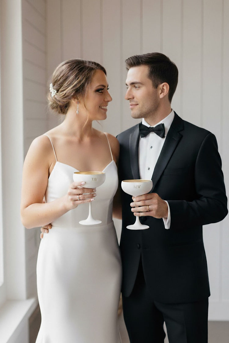 Man and woman in formal attire holding drinks, smiling at each other.